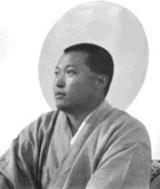 A man in a robe sitting down with his hands crossed.